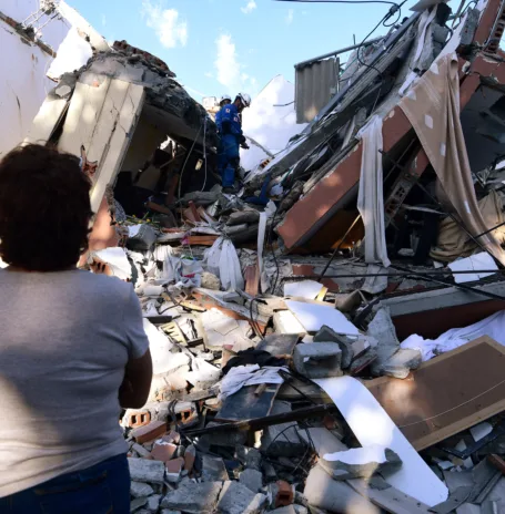 A woman looks at rescuers searching for survivors amid the rubble of a collapsed building after an earthquake in Pereira, Colombia on August 10, 2026. A magnitude 7.4 earthquake struck Colombia on August 10, 2026, and killed at least 111 people, damaged more than 1,500 buildings, and left an unknown number of people buried under rubble. The government declared a state of emergency to attend to the quake that shook several cities across the coffee-producing region, the Pacific coast, and neighboring Latin American countries, sending terrified residents racing into the street. (Photo by Jaime SALDARRIAGA / AFP)
