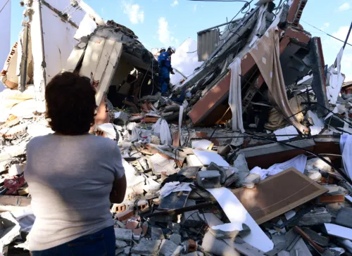A woman looks at rescuers searching for survivors amid the rubble of a collapsed building after an earthquake in Pereira, Colombia on August 10, 2026. A magnitude 7.4 earthquake struck Colombia on August 10, 2026, and killed at least 111 people, damaged more than 1,500 buildings, and left an unknown number of people buried under rubble. The government declared a state of emergency to attend to the quake that shook several cities across the coffee-producing region, the Pacific coast, and neighboring Latin American countries, sending terrified residents racing into the street. (Photo by Jaime SALDARRIAGA / AFP)